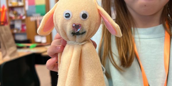 Child holding a handmade plush dog with googly eyes and a heart-shaped nose.