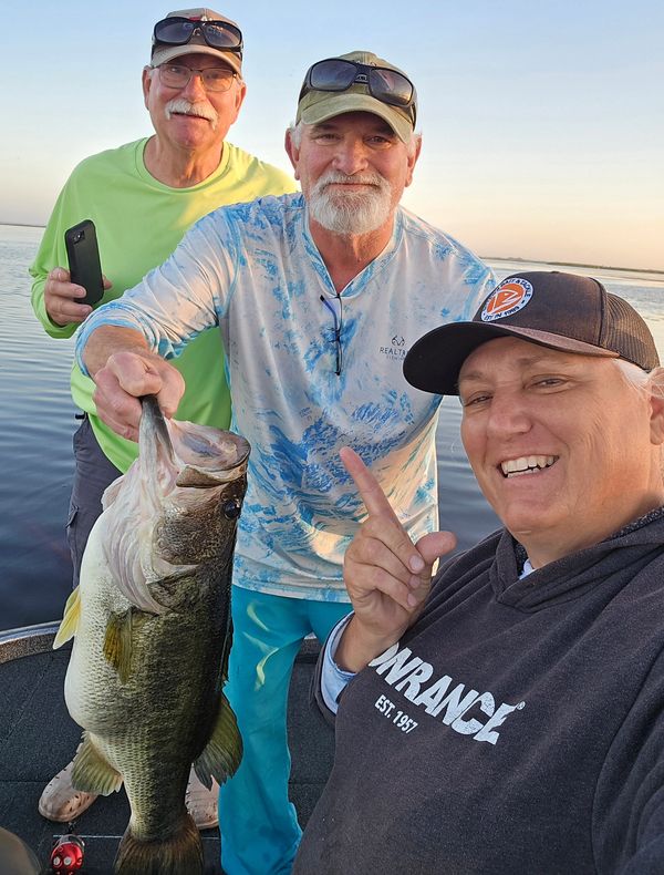 Three people proudly display a large fish caught on a boat.