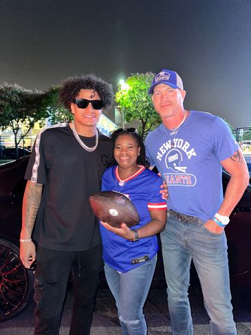 Three people posing with a football at night.