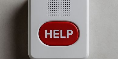 A white emergency help button with a red center on a gray wall.