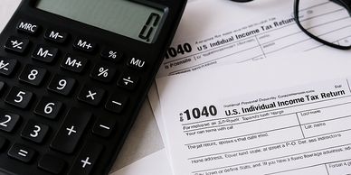Calculator, eyeglasses, and U.S. Individual Income Tax Return forms on a table.