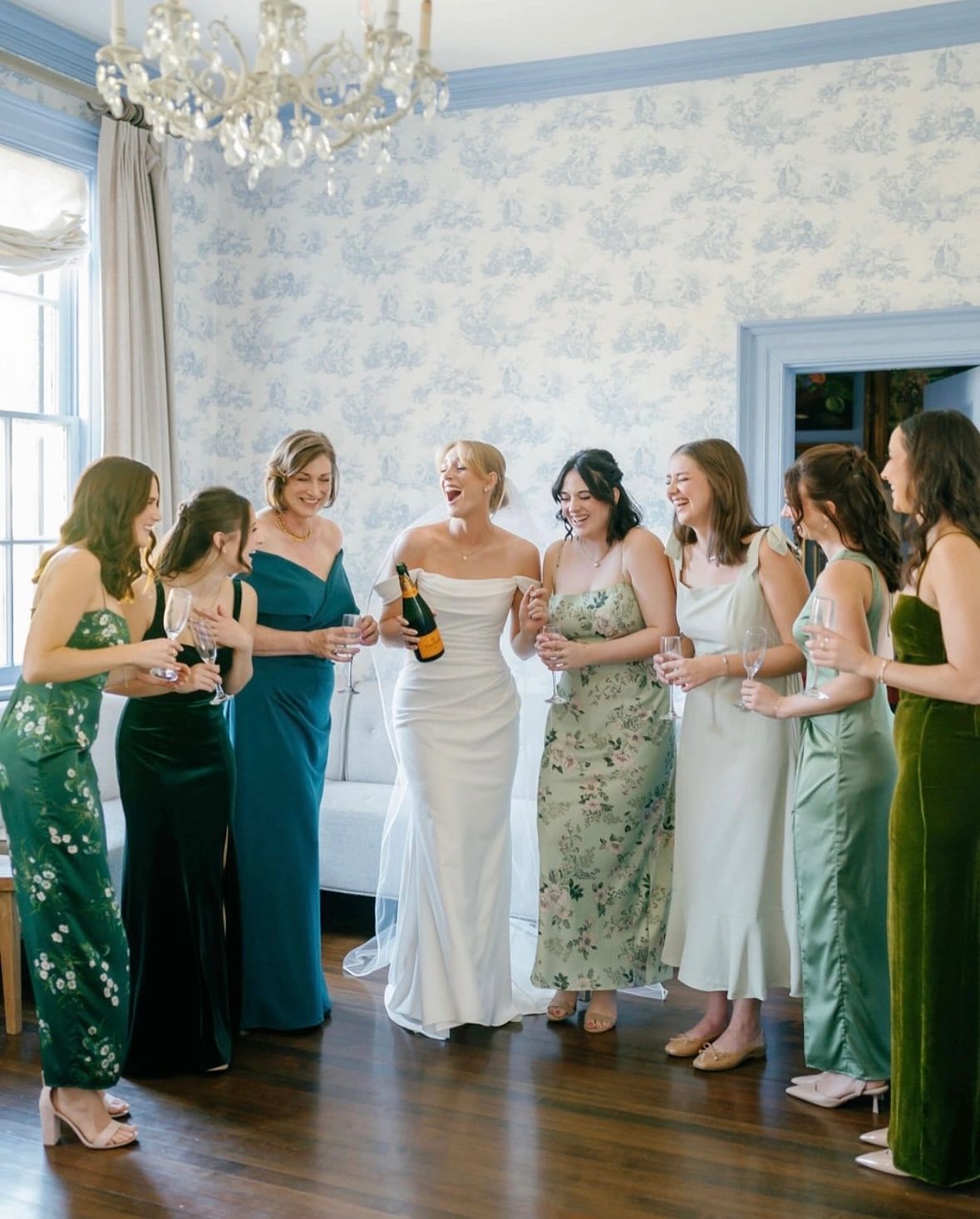 Bride and bridesmaids joyfully celebrating with champagne indoors.