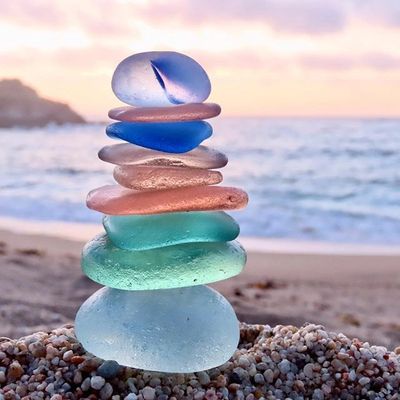 Stack of colorful sea glass stones balanced on a beach during sunset.