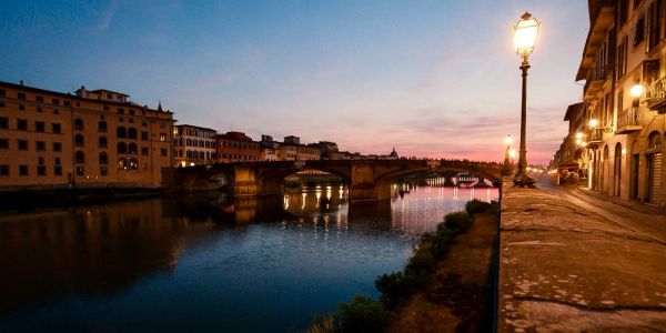 Sunset over a river with a bridge and street lamps.
