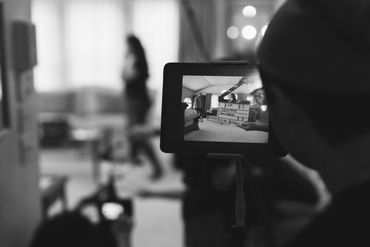 A person filming a scene indoors with a camera monitor showing the setup.