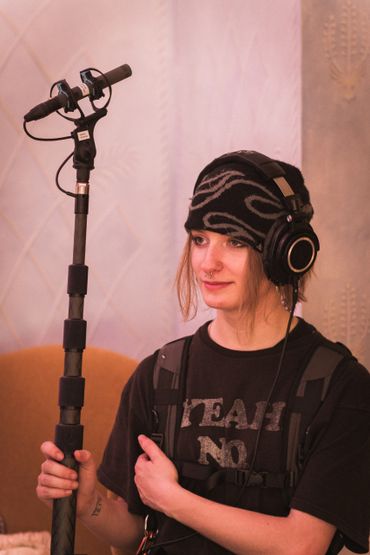 Person wearing headphones and a beanie holding a microphone stand.