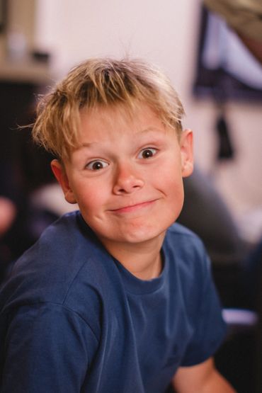 A young boy with a playful expression and tousled hair wearing a blue shirt.