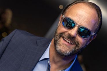 Smiling man wearing sunglasses and a suit jacket.