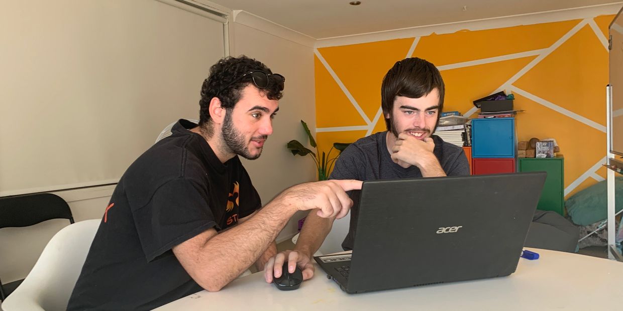 Worker and student seated in front of a laptop. Worker is pointing at screen. 