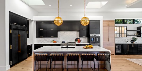 A modern kitchen with black cabinets, marble countertops, and a large island.
