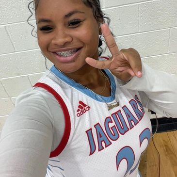 Smiling young woman in Jaguars basketball jersey flashing a peace sign.