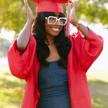 Young woman in red graduation gown smiling outdoors.