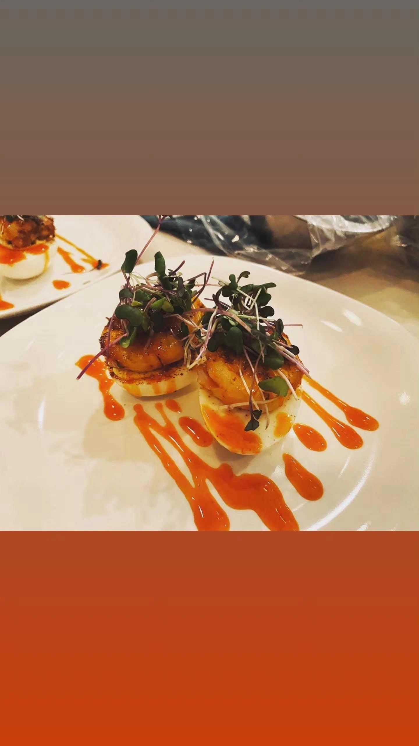 Deviled eggs topped with shrimp, microgreens, and drizzled with hot sauce.