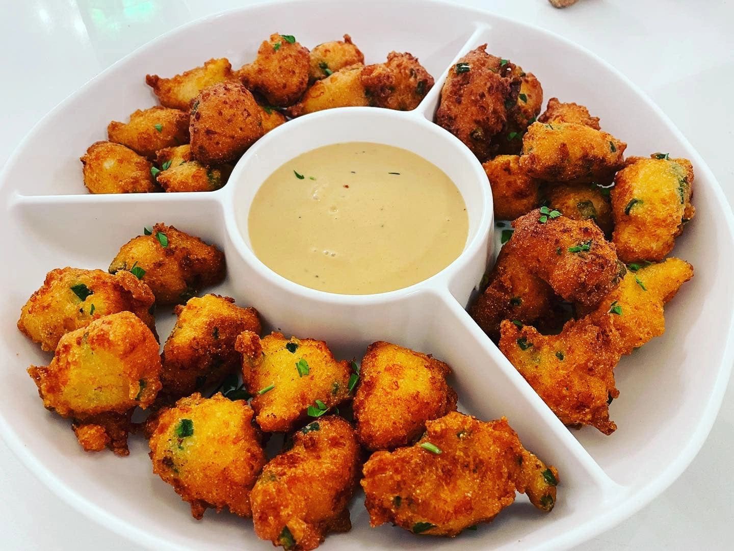 Golden fried fritters served with creamy dipping sauce in a divided dish.