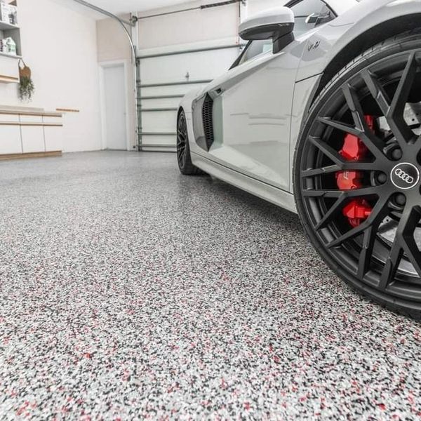 Close-up of a luxury Audi car wheel in a clean garage with speckled epoxy flooring.