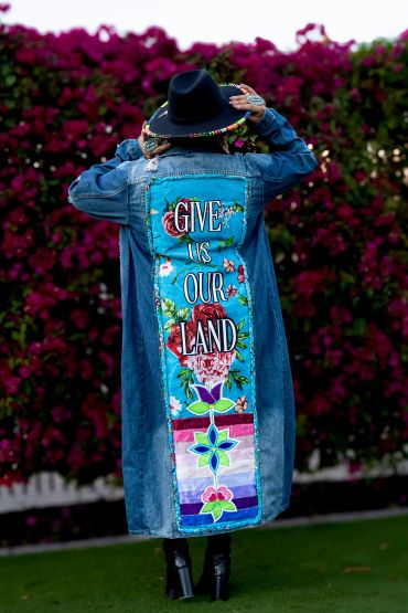 Person wearing a denim jacket with "Give Us Our Land" message.