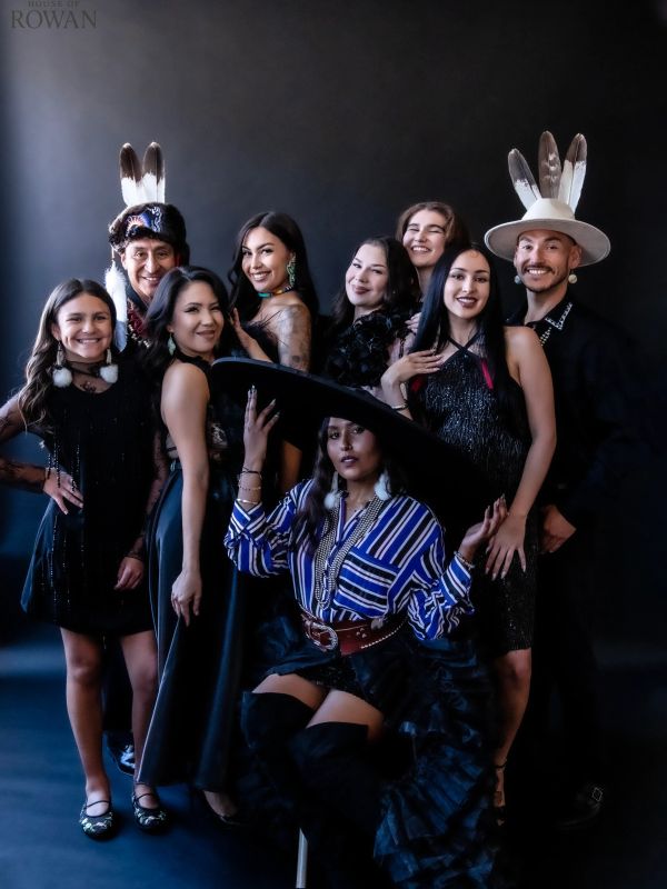 Group portrait of nine people in stylish attire with feathered headwear.