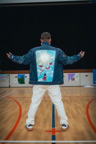 Person in a denim jacket with artwork on back in a gym.