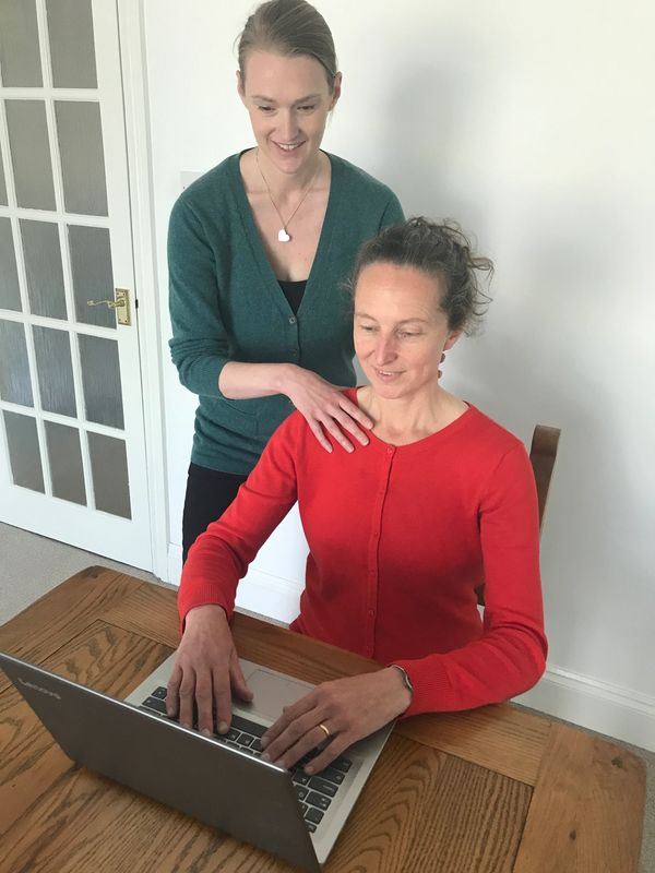 Natalie working hands on with a client who is using a laptop. Natalie touching neck and shoulder.