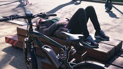 Picture of person lying on a bench doing some Constructive Rest next to thier bike. 