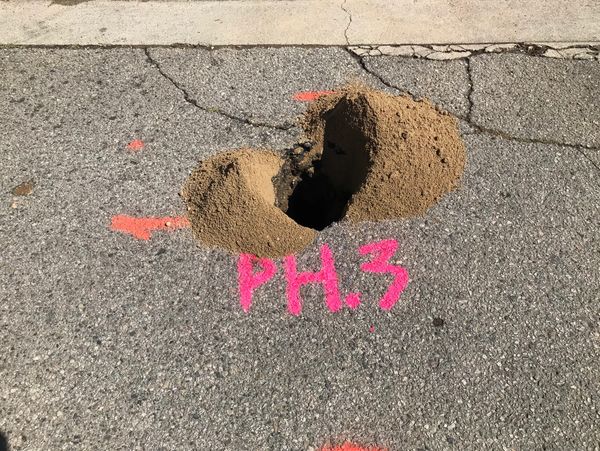 Small hole in asphalt with orange markings and dirt piles.