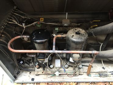 Two compressors connected with copper piping in an industrial setup.