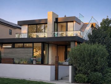 Modern two-story house with large glass windows and rooftop stairs.