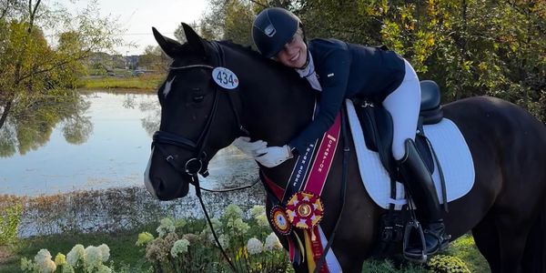 Equestrian champion hugging a horse by a lake.