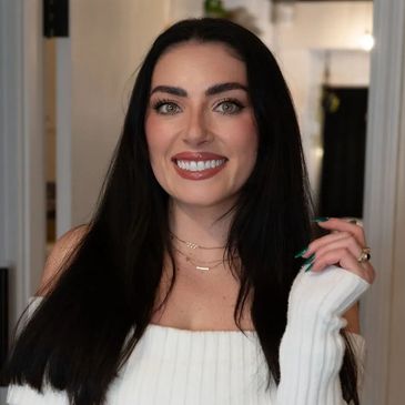 Smiling woman with long dark hair wearing a white off-shoulder sweater.