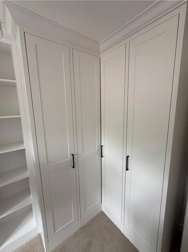 White corner wardrobe with black handles and adjacent shelving unit.