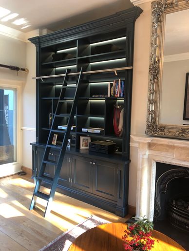 A tall black bookshelf with a sliding ladder in a cozy room.
