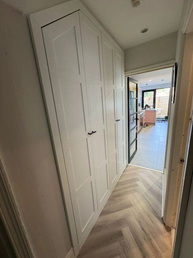 White built-in closets in a narrow hallway leading to a bright kitchen.
