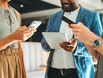 Three people using smartphones and a tablet in a casual business setting.