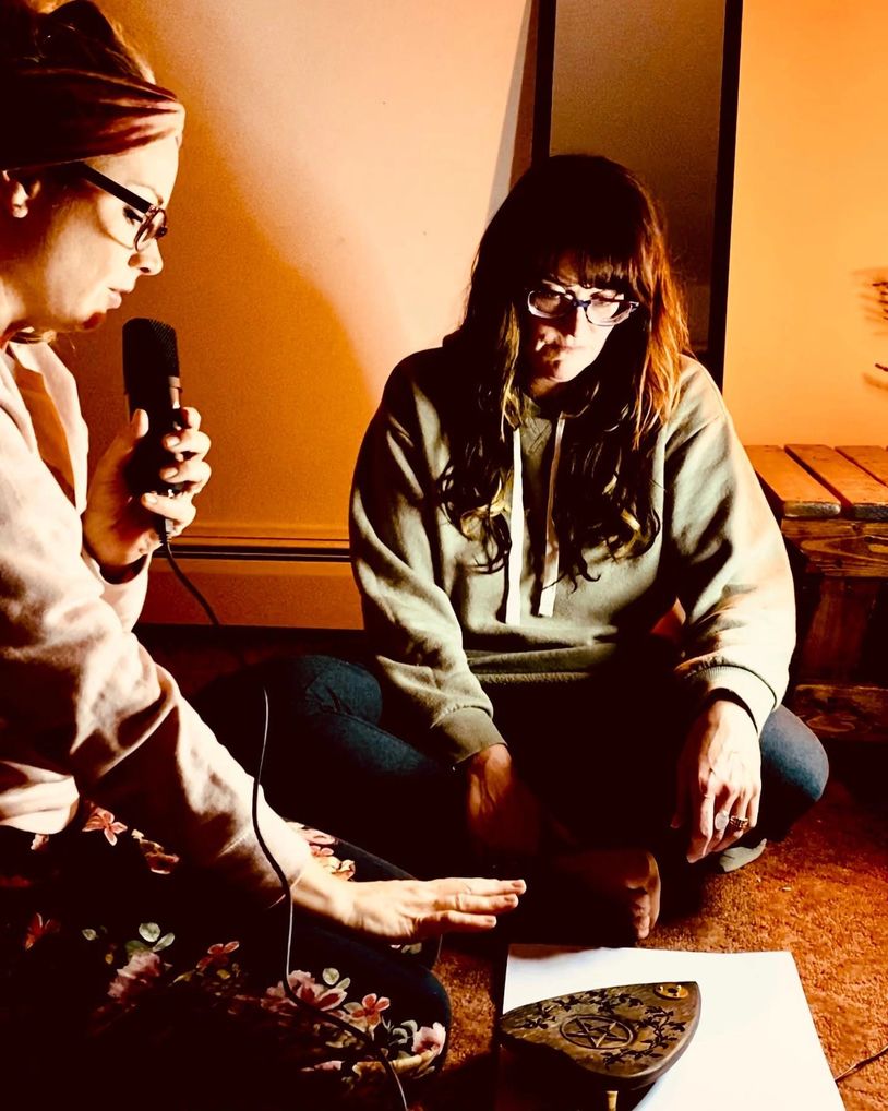 two woman sitting in a room with a microphone recording a podcast
