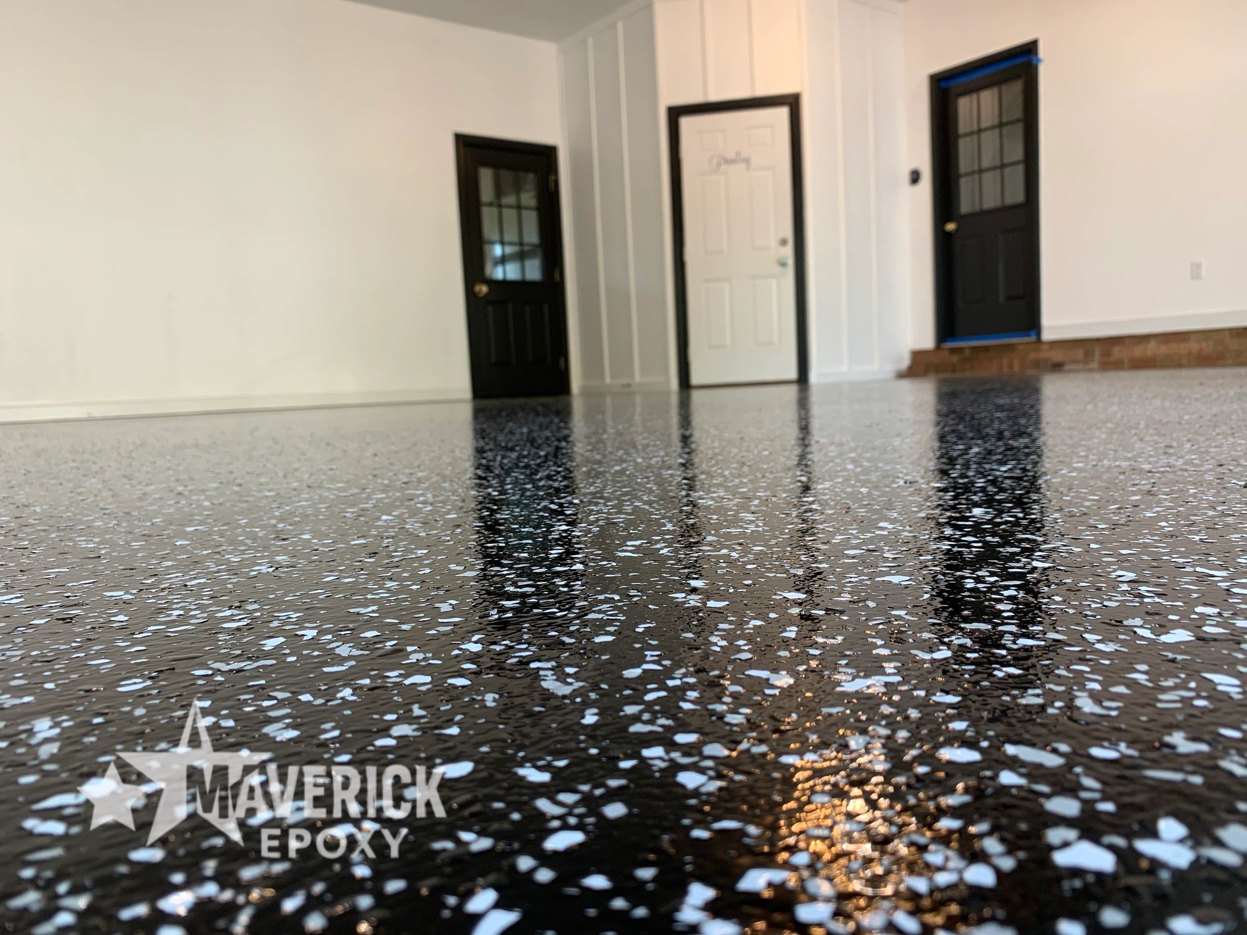 Shiny black epoxy floor with white flakes and three doors in the background.