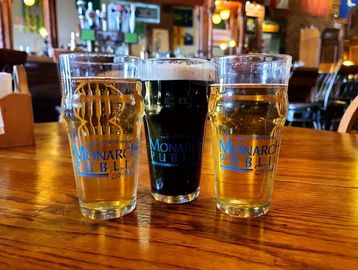 Three glasses of Monarch Pub beer on a wooden bar counter.