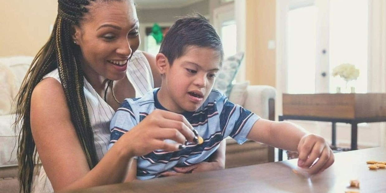 A special needs mom helping her son at the kitchen table.