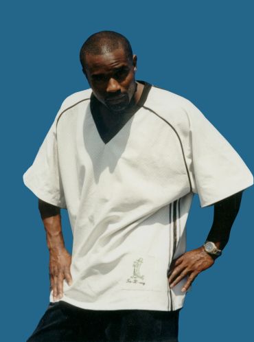 Man posing in a loose white shirt against a blue background.