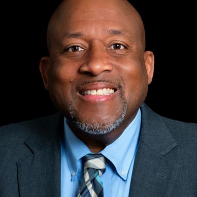 Smiling man in suit and tie against a black background.