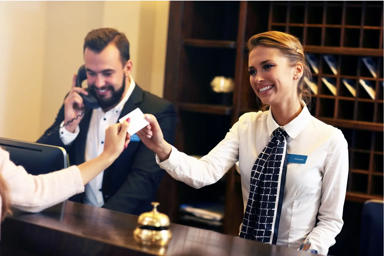 Two receptionists handing a hotel card to a guest