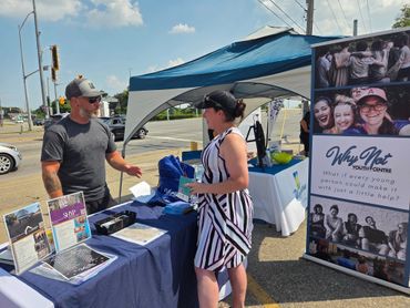 Two people conversing at an outdoor booth with promotional displays.