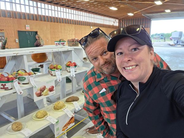 Two people smiling at a fruit and vegetable display.