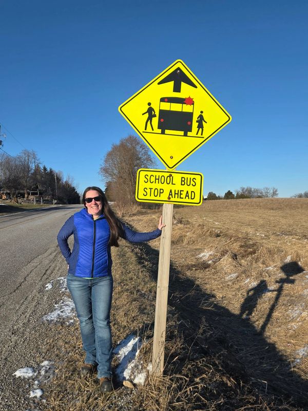 Woman standing next to a school bus stop sign on a sunny day.