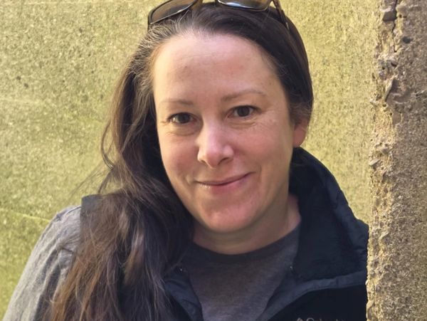 Woman with long brown hair smiling outdoors.