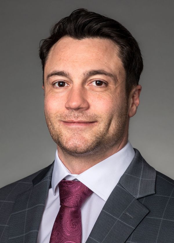 Professional man in suit and patterned tie smiling subtly.