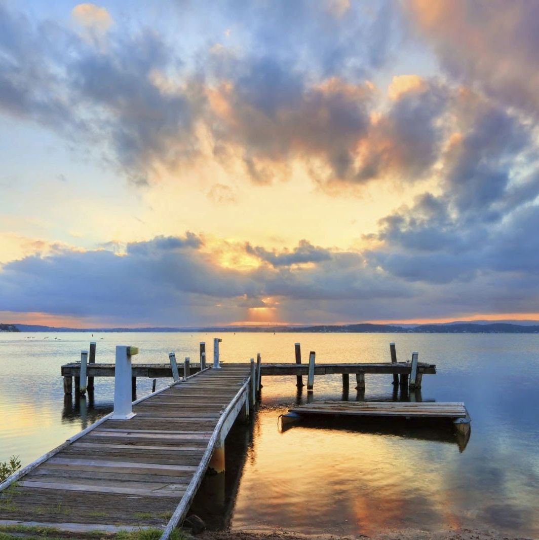 Wooden pier extending into calm lake during sunset with dramatic clouds.