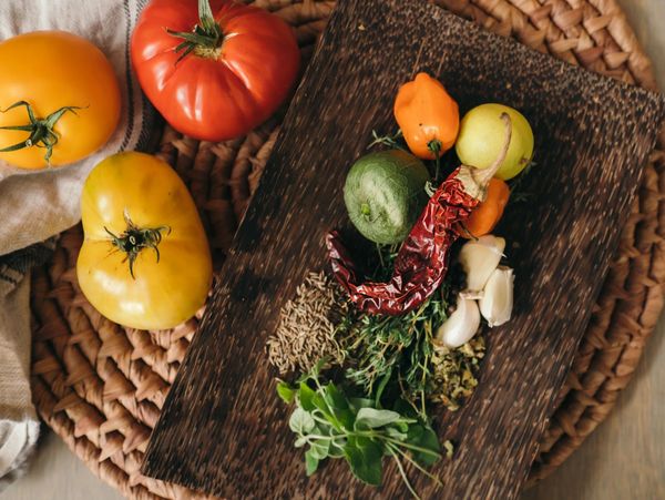 Fresh herbs, spices, and colorful tomatoes arranged on a rustic wooden board.