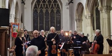 Musicians with string instruments standing in a church, acknowledging the audience.