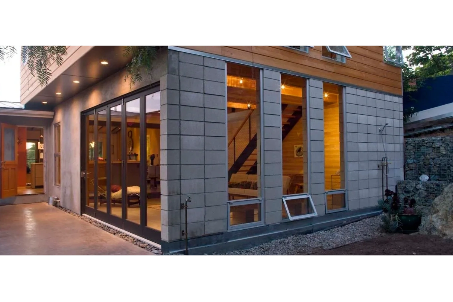 Modern house exterior with large glass windows and warm interior lighting.