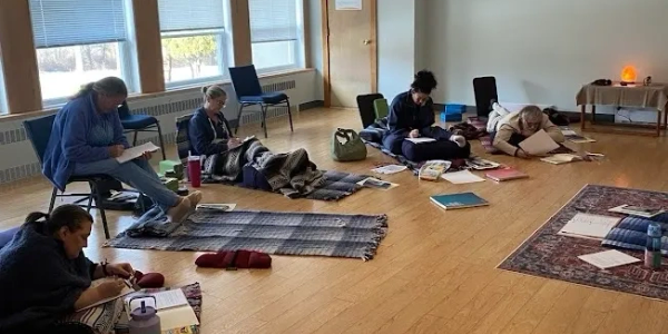 People engaged in study or relaxation on mats and chairs in a bright room.